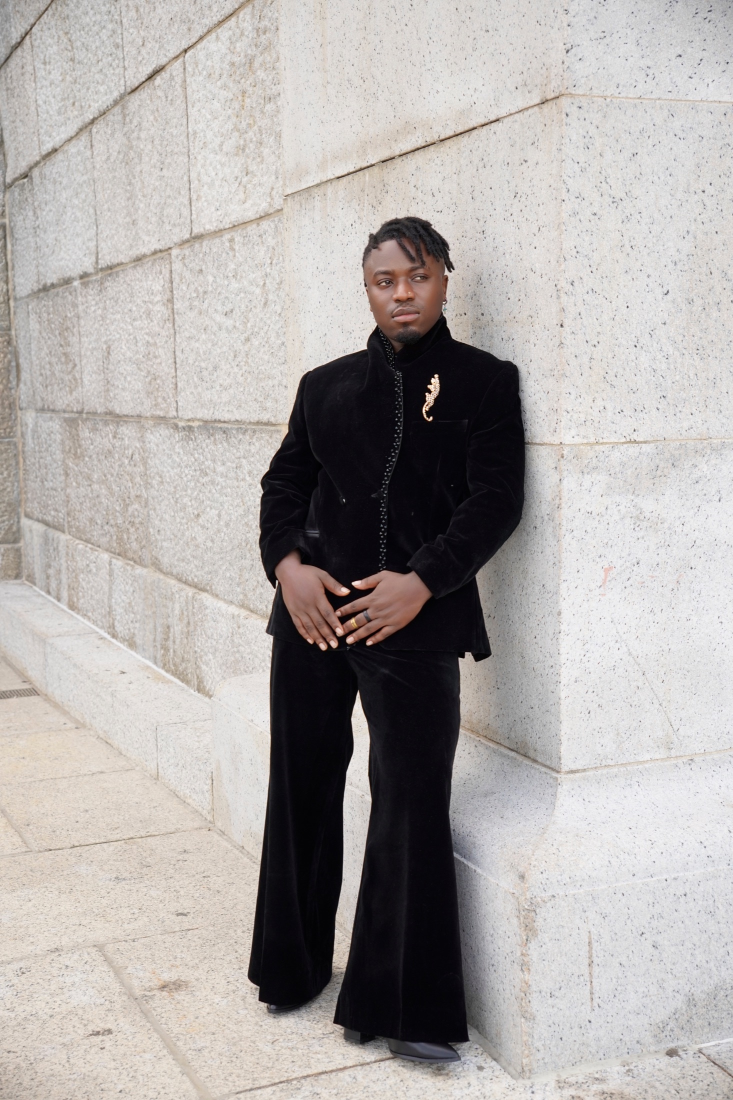 Full-length portrait in black velvet against a stone wall